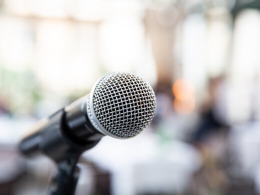 Ein Mikrofon vor einem unscharfen Hintergrund symbolisiert eine Pressekonferenz.