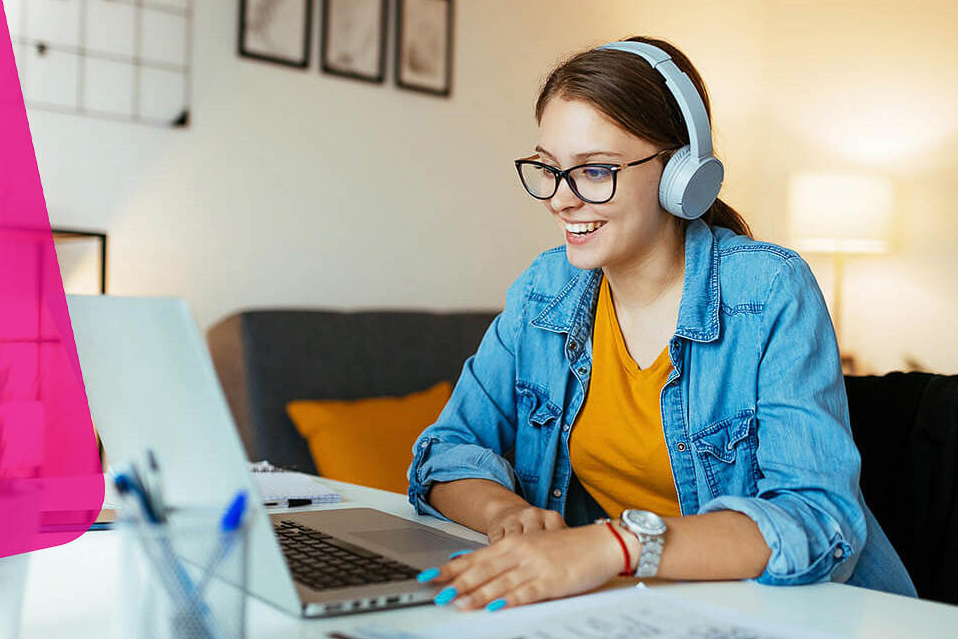 Eine Frau sitzt lächelnd mit einem Headset vor ihrem Computerbildschirm.